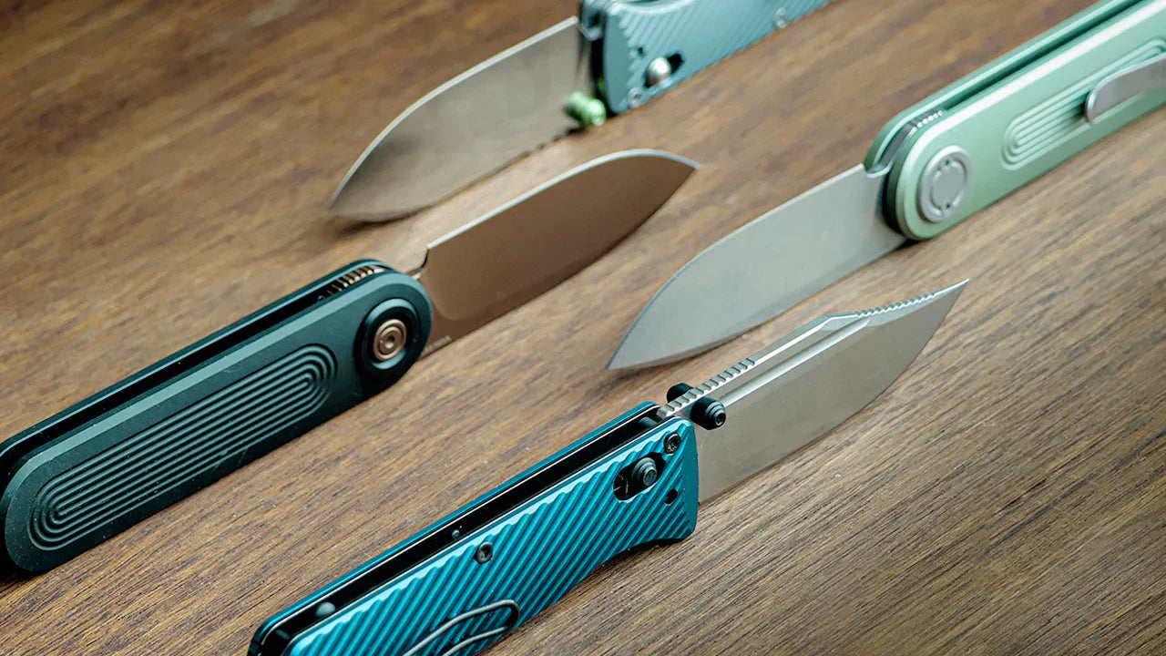 Four folding pocket knives with teal/turquoise handles displayed open on a wooden surface, showing their stainless steel blades