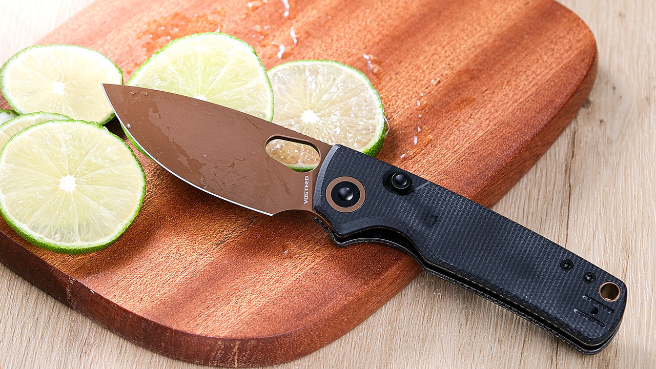 Vosteed pocket knife with a dark handle and bronze-colored blade resting on a wooden cutting board next to sliced limes, highlighting its design and potential use