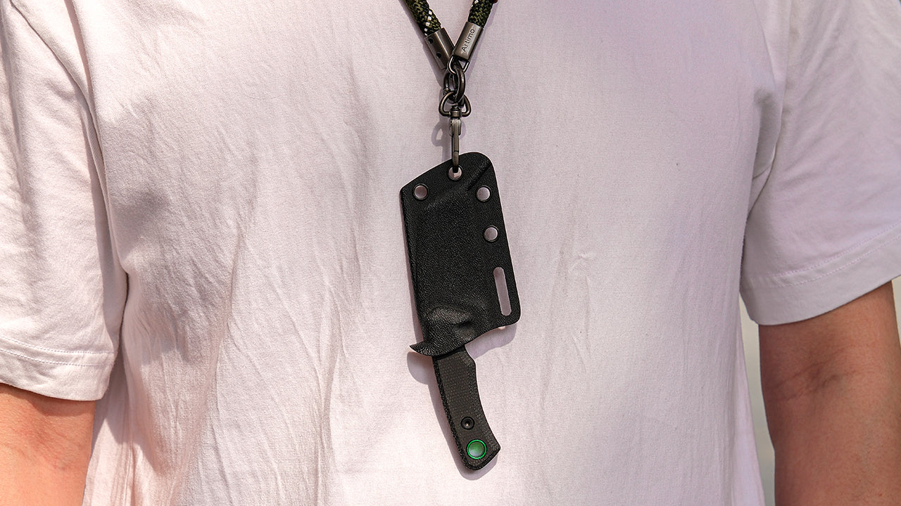 Neck knife suspended from neck - Small fixed blade in black Kydex sheath hanging from cord system on white t-shirt, demonstrating neck carry method