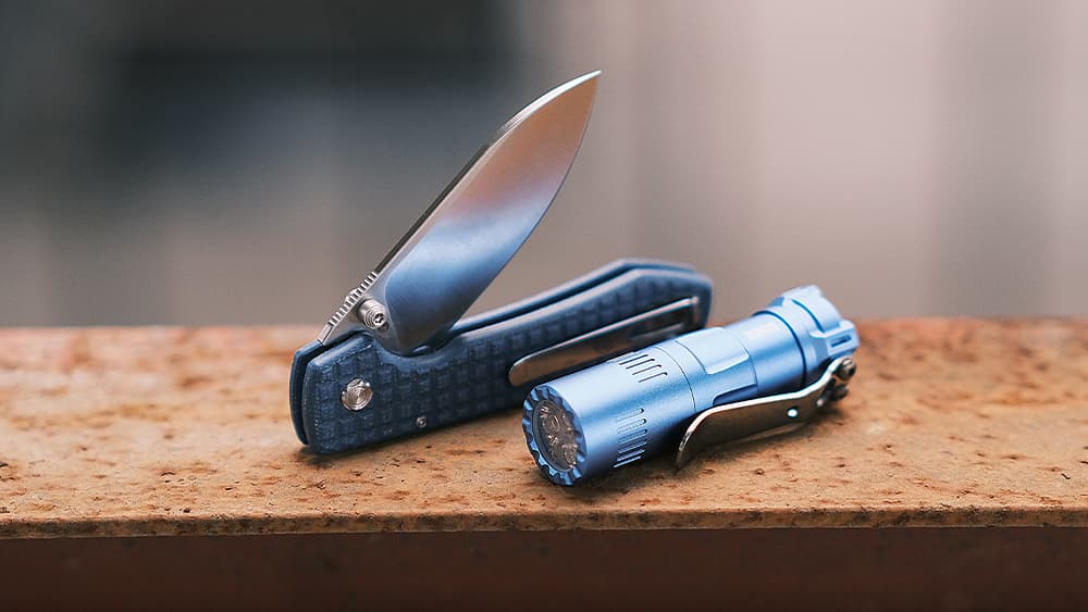 Vosteed EDC Combination: A folding knife with a blue carbon fiber handle and a matching blue EDC flashlight placed on a rusty metal surface