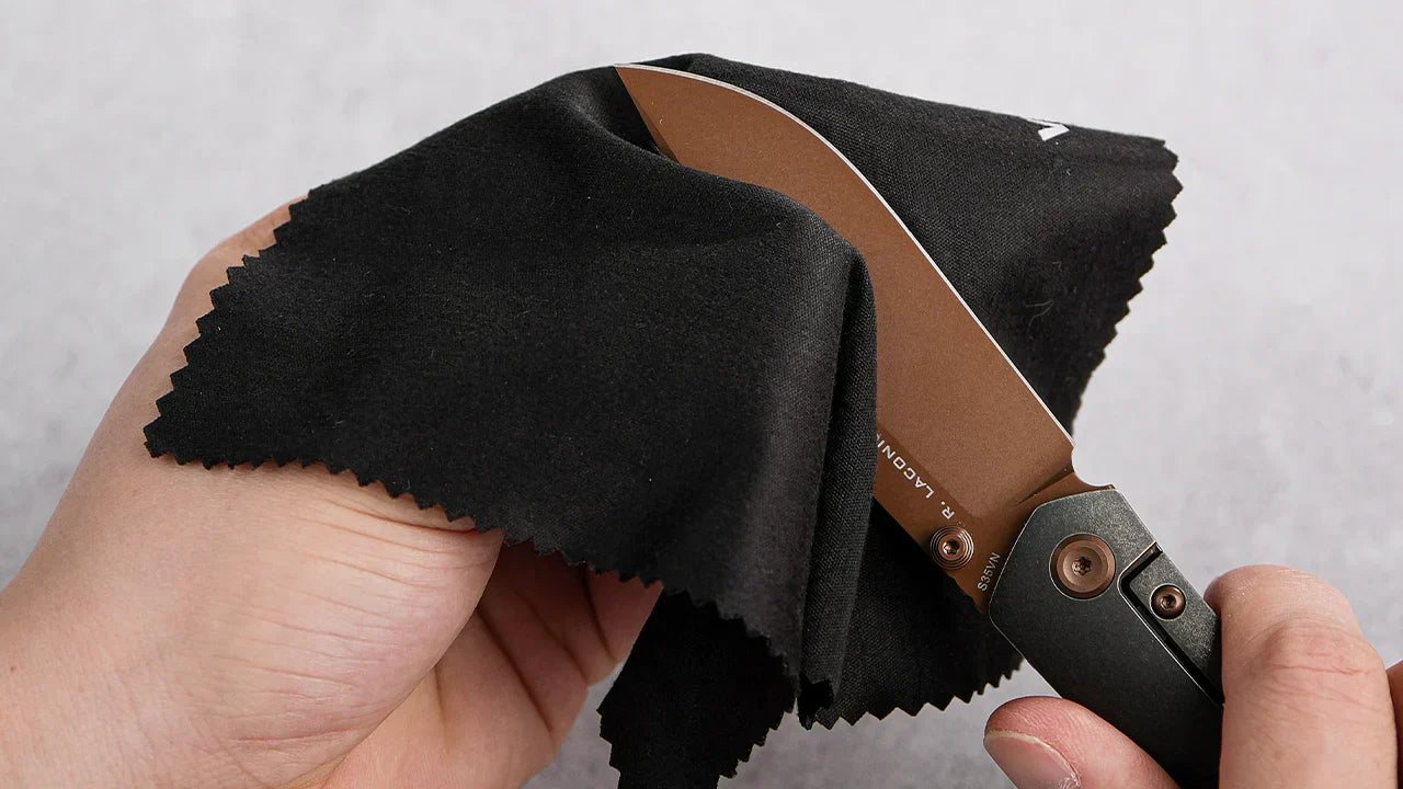A hand wiping a knife blade with a black cleaning cloth