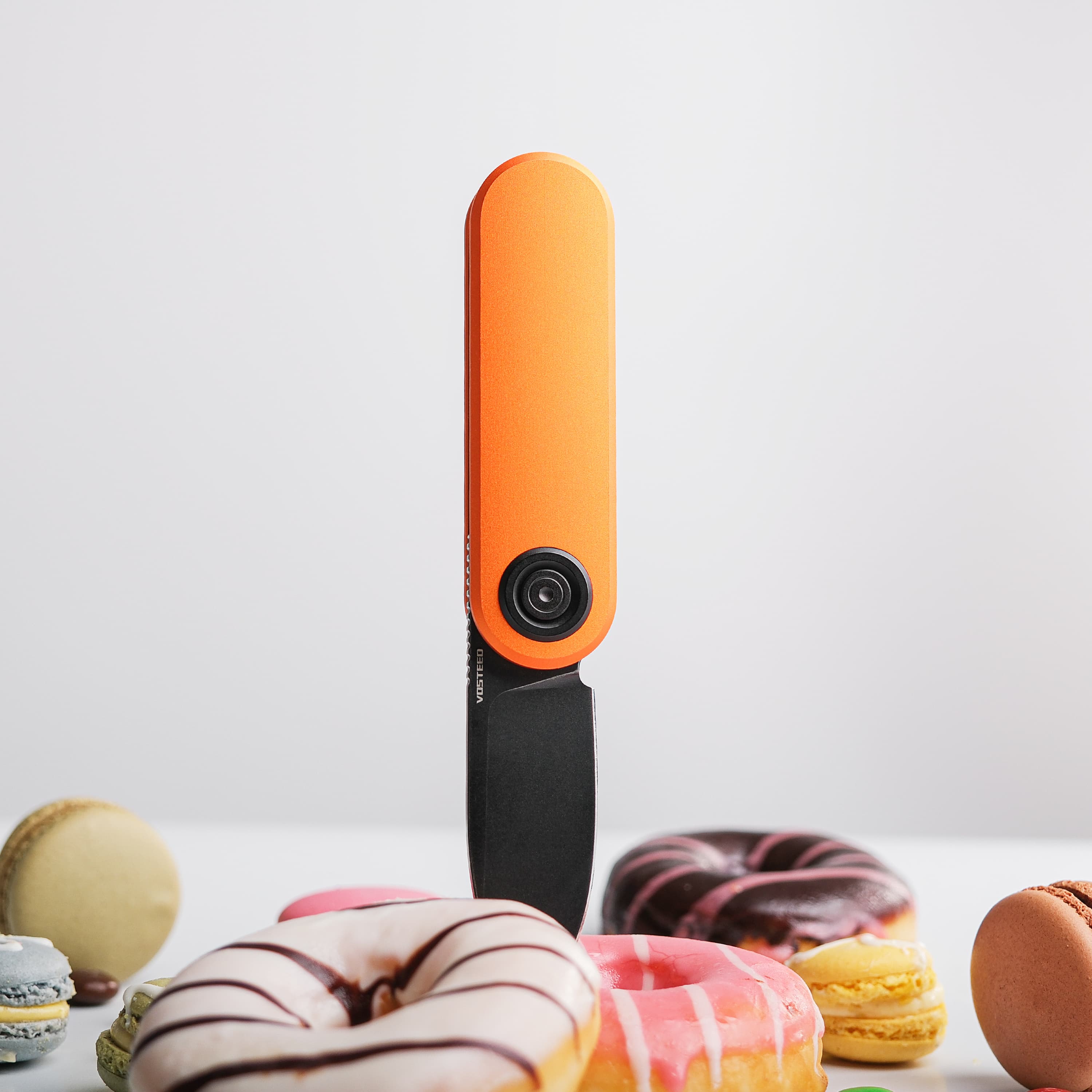 Vosteed Corgi V knife with orange handle among desserts