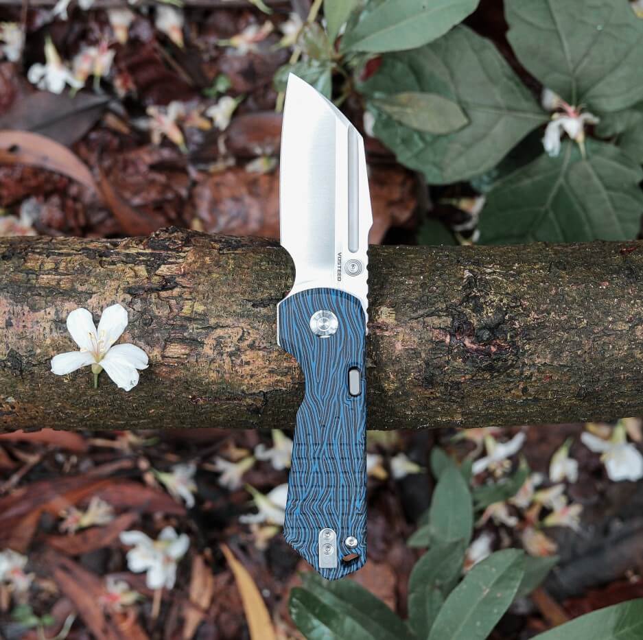 Vosteed Hedgehog knife on a log, blade open, blue handle, forest backdrop