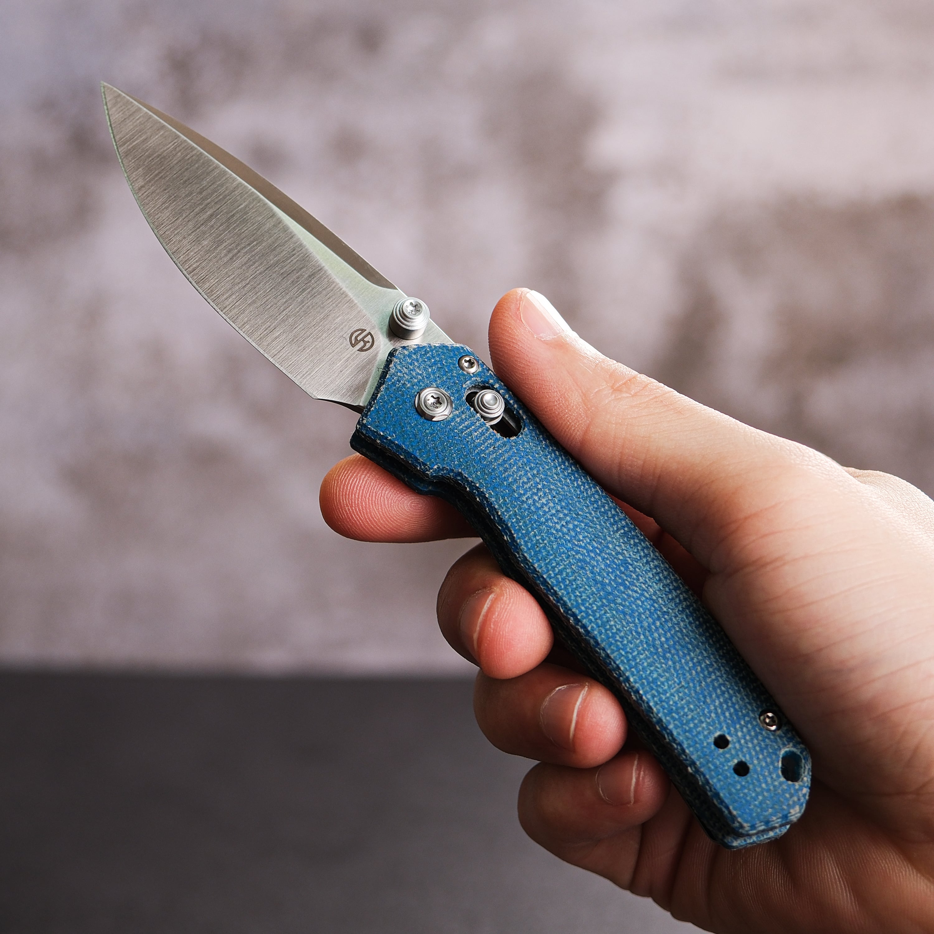 Vosteed Mini Psyop knife with blue Micarta handle, held in hand
