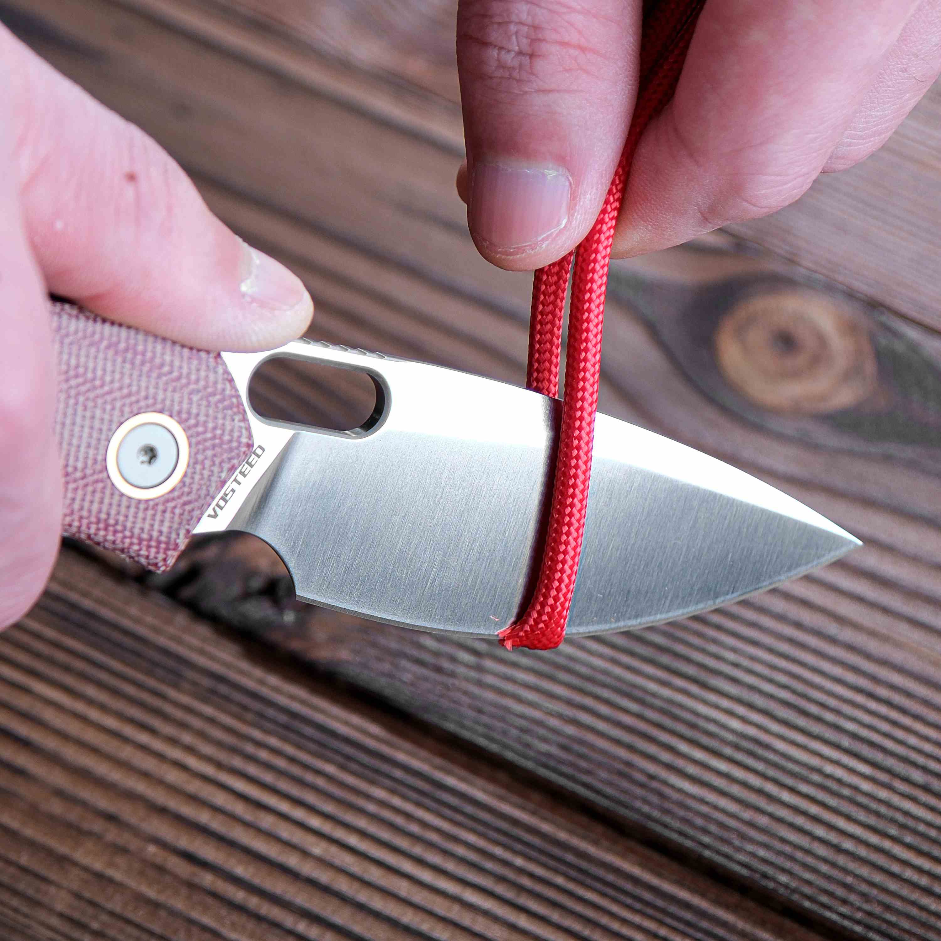 Vosteed Psyop knife cutting red cord, showing blade sharpness