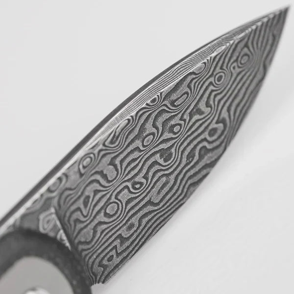 Close-up of a Damascus steel knife blade showing distinctive wavy pattern formed by layers of folded steel. The blade features intricate swirling patterns characteristic of Damascus forging techniques