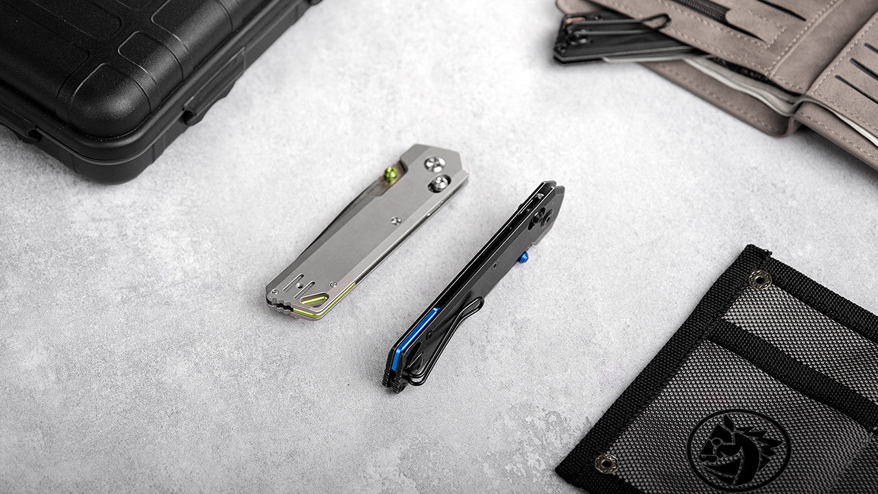 Close-up of two lightweight folding knives - one silver metallic knife and one black knife with blue accents - placed on a gray surface with a black mesh storage pouch nearby, demonstrating the minimalist design of modern EDC knives